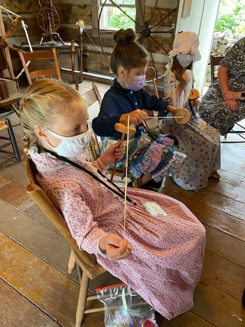Elementary students in 1800s clothing spin yarn