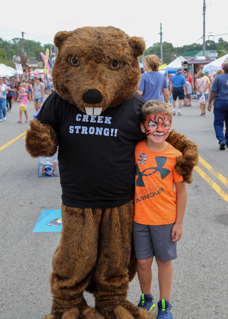 Boy with tiger face paint poses with Bucky the Beaver mascot 