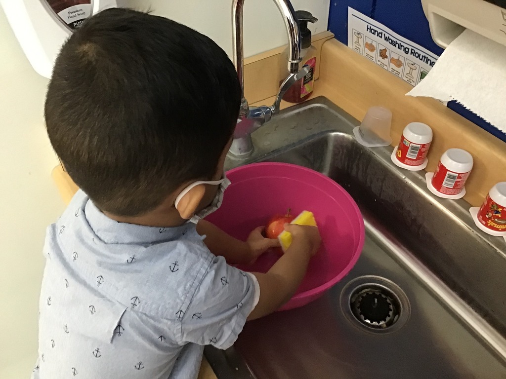 Preschooler washes apple in sink