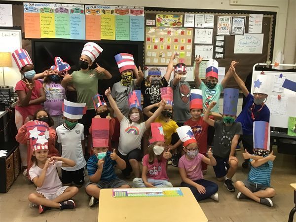 Students wearing handcrafted USA hats give thumbs-up