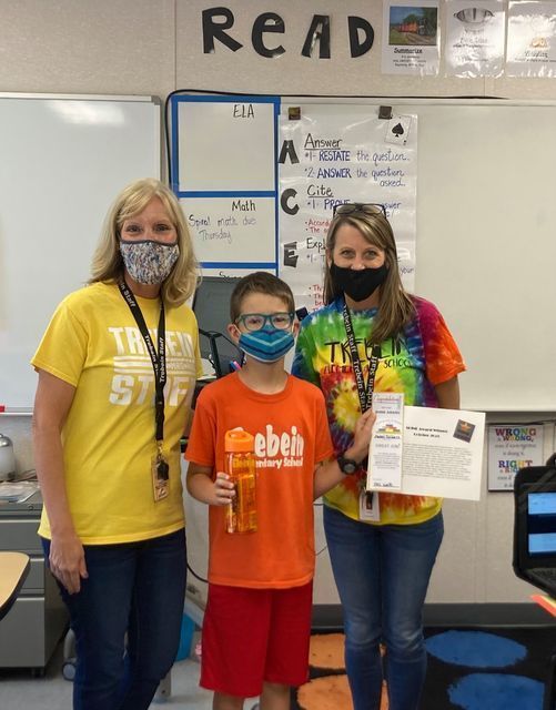 5th grader poses with a certificate and his teachers in classroom