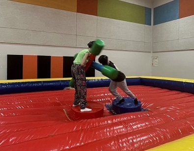 Two kids playing king of the mountain on a blow up arena