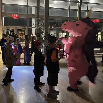 Student in costumes dancing.  One is a an inflatable pink unicorn