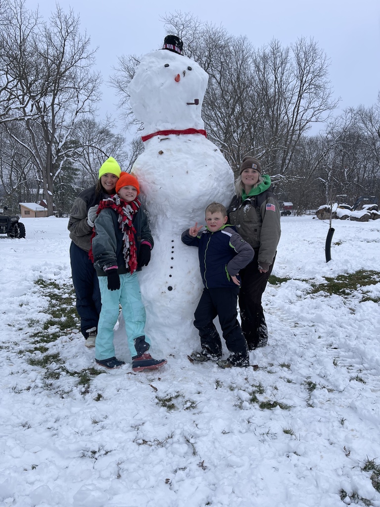 4 students standing beside a snowman taller than they are. 