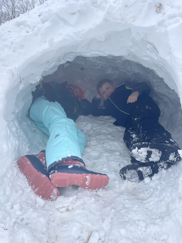 Two students laying inside an igloo shaped snow fort