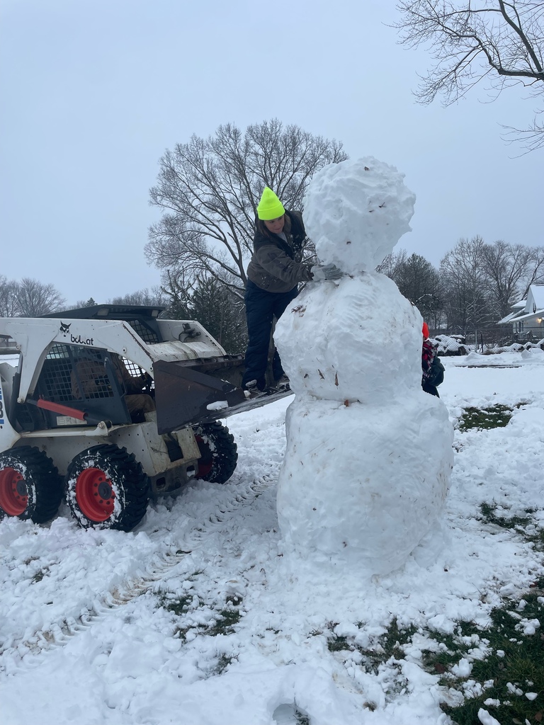 Parent on a the basket of small bulldozer putting the head on a really tall snowman. 